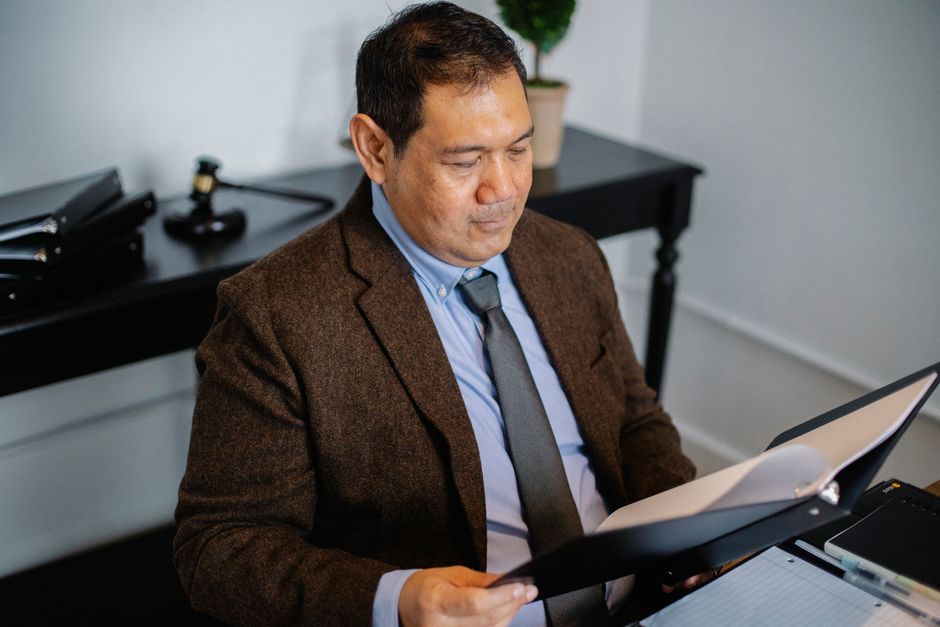 From above of serious ethnic lawyer in elegant suit checking report in folder on blurred background of office