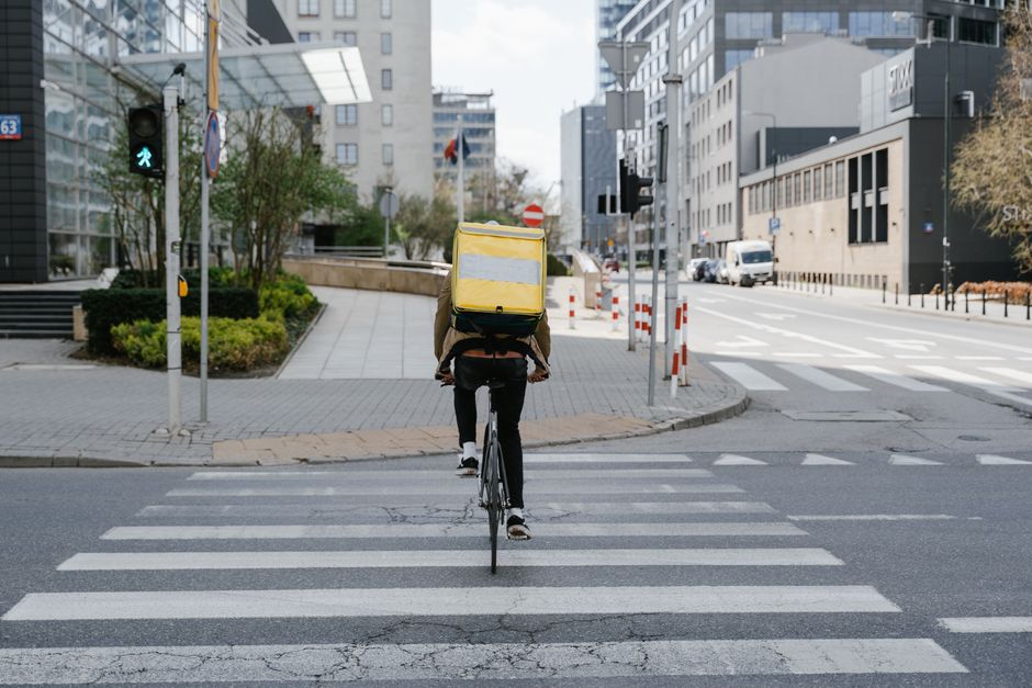 California Employee Misclassification 5 Cyclist with thermal bag crossing street in downtown Warsaw, Poland.